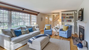A living room with a sofa, two armchairs, a fireplace, a bookshelf, and a staircase. - Expansive Group Getaway < 1 Mi to Dtwn Falmouth! (Falmouth)