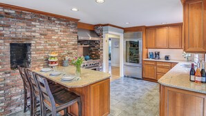 A kitchen with a brick wall, wooden cabinets, granite countertops, and a central island. - Expansive Group Getaway < 1 Mi to Dtwn Falmouth! (Falmouth)