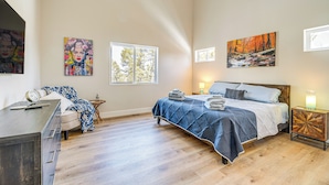 Ein Schlafzimmer mit einem Bett, einem Schreibtisch und einem Deckenventilator. Es gibt Fenster und Gemälde an den Wänden.