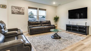 A living room with a leather sofa, a glass coffee table, a black entertainment unit, and a large TV on the wall. - Quiet Avon Home - Near Indianapolis Speedway! (Avon)