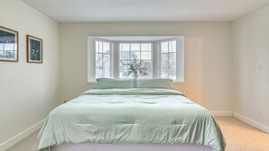 Ein Schlafzimmer mit einem großen Bett, einem Fenster mit Jalousien und einer kleinen Pflanze auf der Fensterbank.