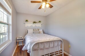 A bedroom with a bed, a nightstand, a ceiling fan, a window, and a shelf with plants. - Pet-friendly Shenandoah Cabin w/ Fire Pit & Grill! (Shenandoah)