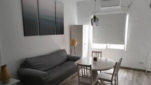 Een moderne woonkamer met een grijze bank, een ronde eettafel met witte stoelen en een hangende吊灯.