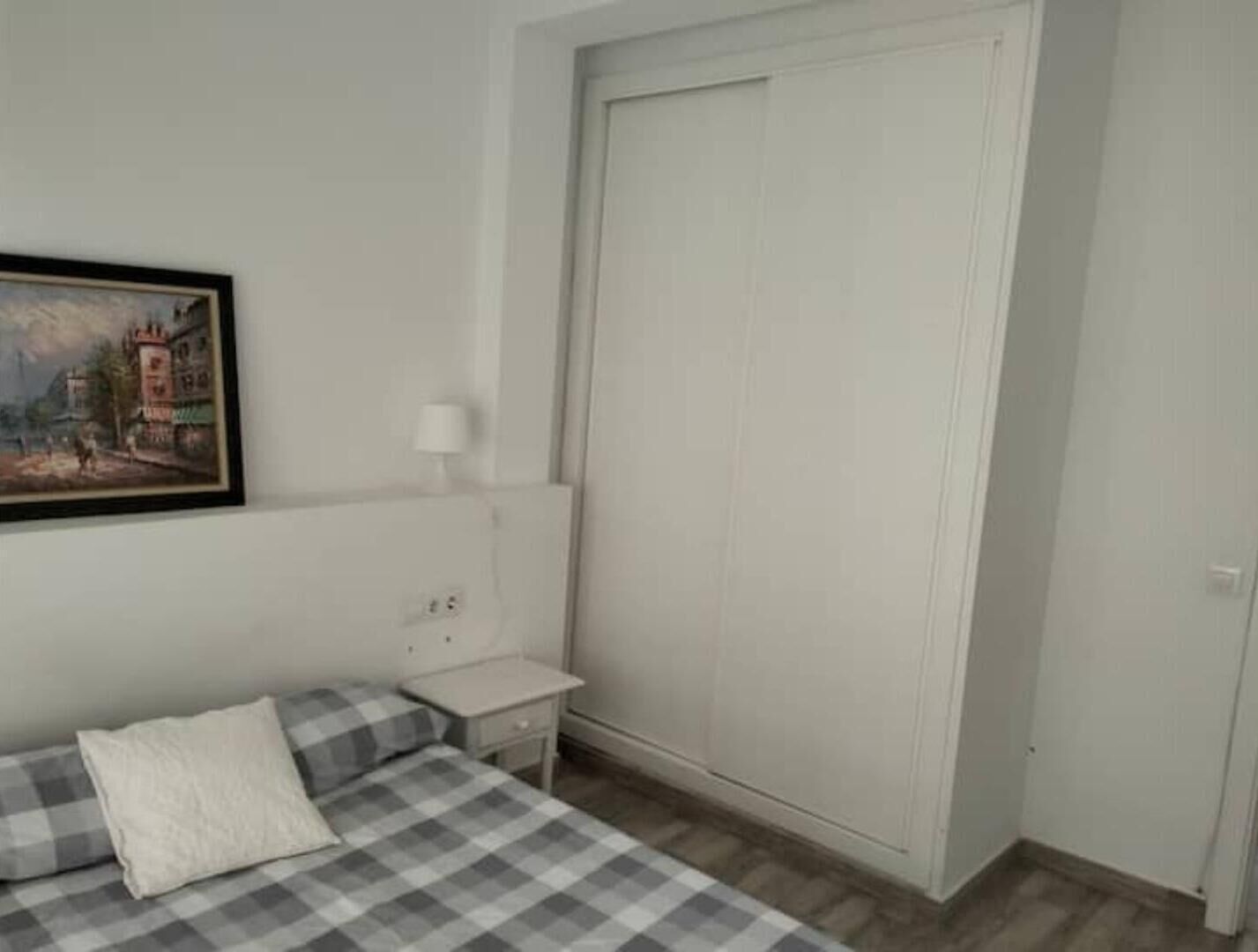 Een slaapkamer met een bed, nachtkastje, lamp, schilderij en een kledingkast.