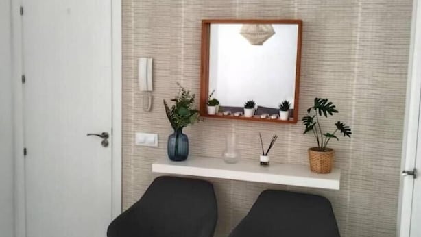 Een kamer met een witte deur, twee zwarte stoelen, een witte plank met decoratieve objecten, en een structuurmuur.