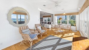 A spacious room with a large window offering a view of the sea, a round mirror on the wall, wicker furniture, and a ceiling fan. - Minnow Mansion 2804 E Co Hwy 30a 3 Bedroom Home by RedAwning (Santa Rosa Beach)