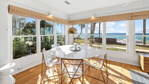 A sunlit room with a round table, clear chairs, and large windows offering a view of the ocean and greenery. - Minnow Mansion 2804 E Co Hwy 30a 3 Bedroom Home by RedAwning (Santa Rosa Beach)