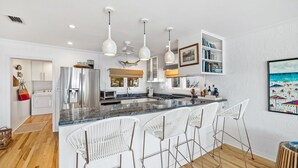 A modern kitchen with a central island, white bar stools, pendant lighting, and a view of the living area. - Minnow Mansion 2804 E Co Hwy 30a 3 Bedroom Home by RedAwning (Santa Rosa Beach)