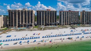 A beachfront hotel with multiple high-rise buildings, a sandy beach with umbrellas, and a pool area.