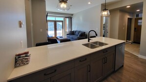 A modern kitchen with a large island, a built-in sink, and wooden cabinets. - Powder Heights #22 2 Bedroom Townhouse (Sun Peaks)