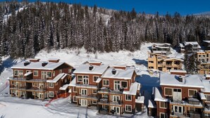 A snow-covered resort with multiple two-story buildings, each with balconies and large windows. - Powder Heights #22 2 Bedroom Townhouse (Sun Peaks)