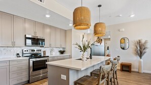 Cozinha moderna com eletrodomésticos de aço inoxidável, uma ilha central com banquetas e iluminação pendente.