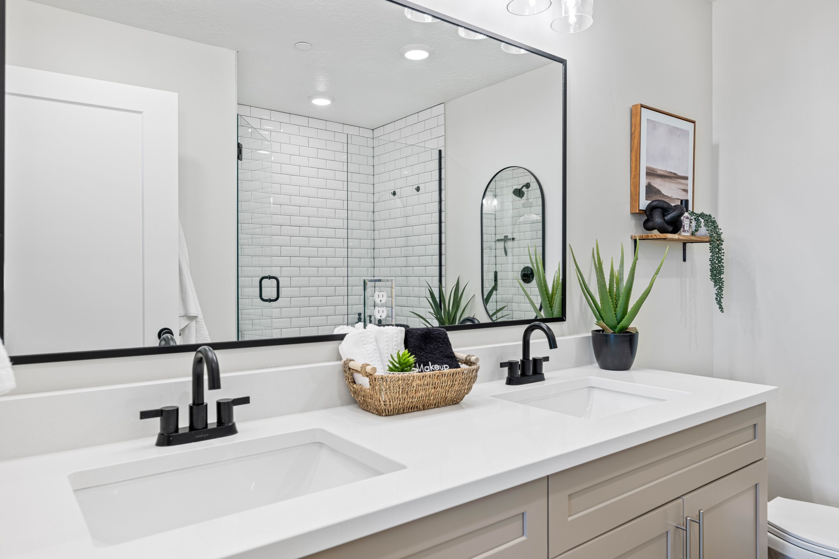 A modern bathroom with a large mirror, two sinks, and a vanity with drawers.