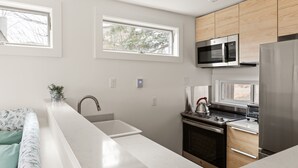 A modern kitchen with a large island, wooden cabinets, stainless steel appliances, and two windows providing natural light. - 22 Village Run 3 Bedroom Condo by RedAwning (Warren)
