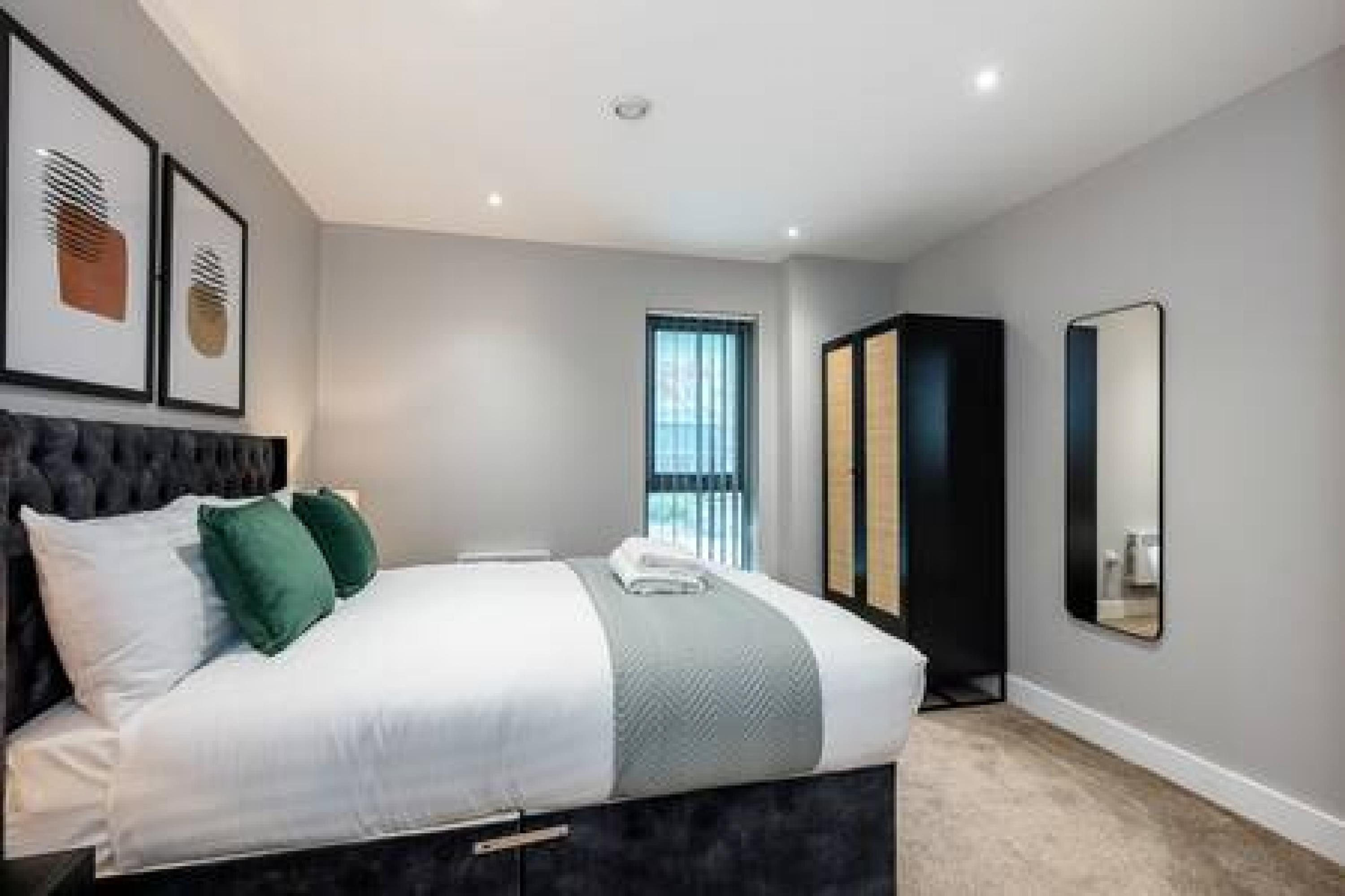A modern bedroom with a bed, a large mirror, and artwork on the wall.