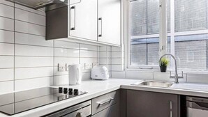 A modern kitchen with white cabinets, a stainless steel countertop, a built-in oven, and a window with blinds. - Host Stay Slater Street Apartments (Liverpool)