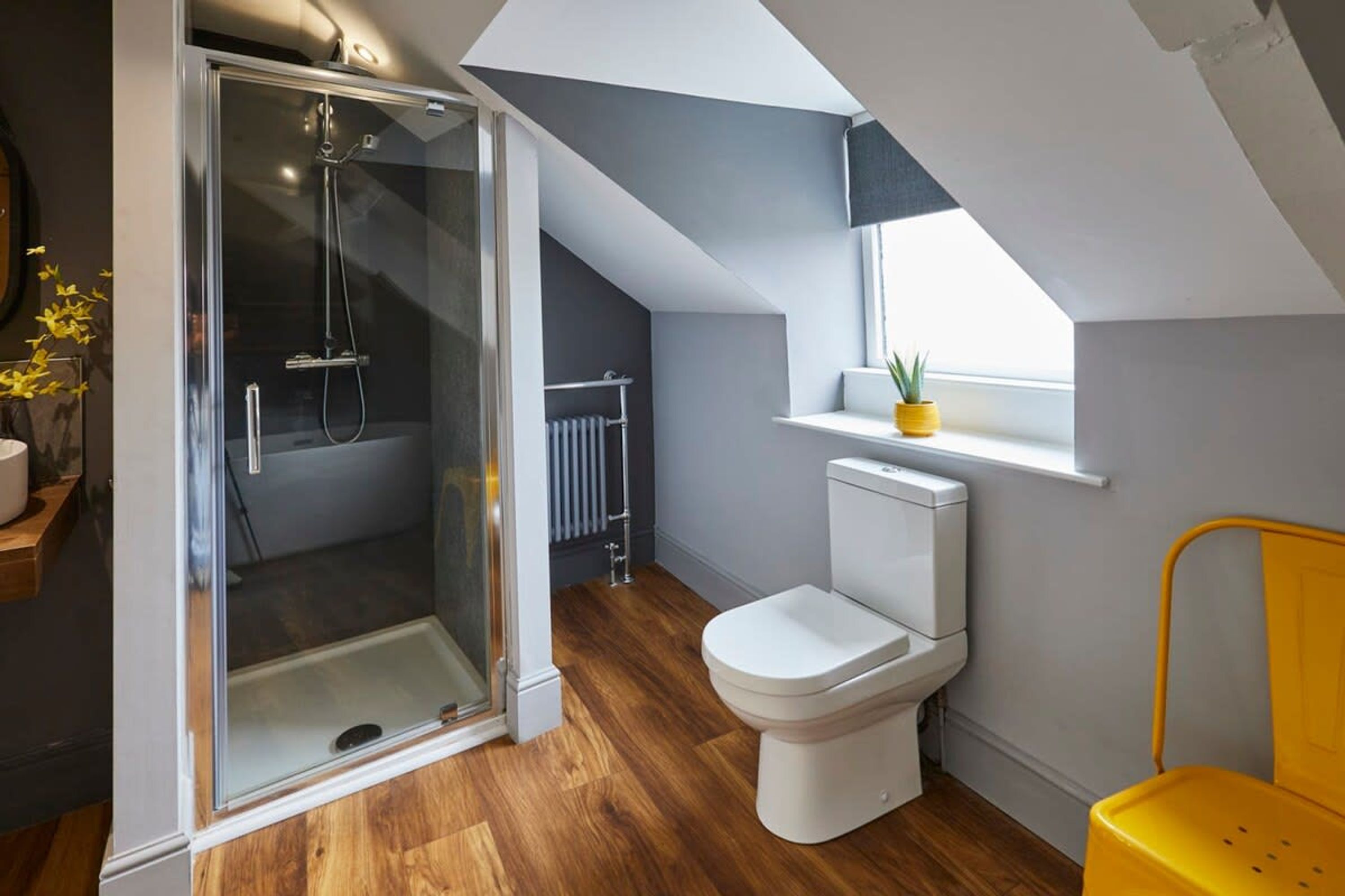 A modern bathroom with a glass shower enclosure, a white toilet, and a yellow chair.