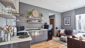 A modern kitchen with a central island, built-in appliances, and a dining area with a sofa and coffee table. - Host Stay Rooftops Grey (Alnwick)