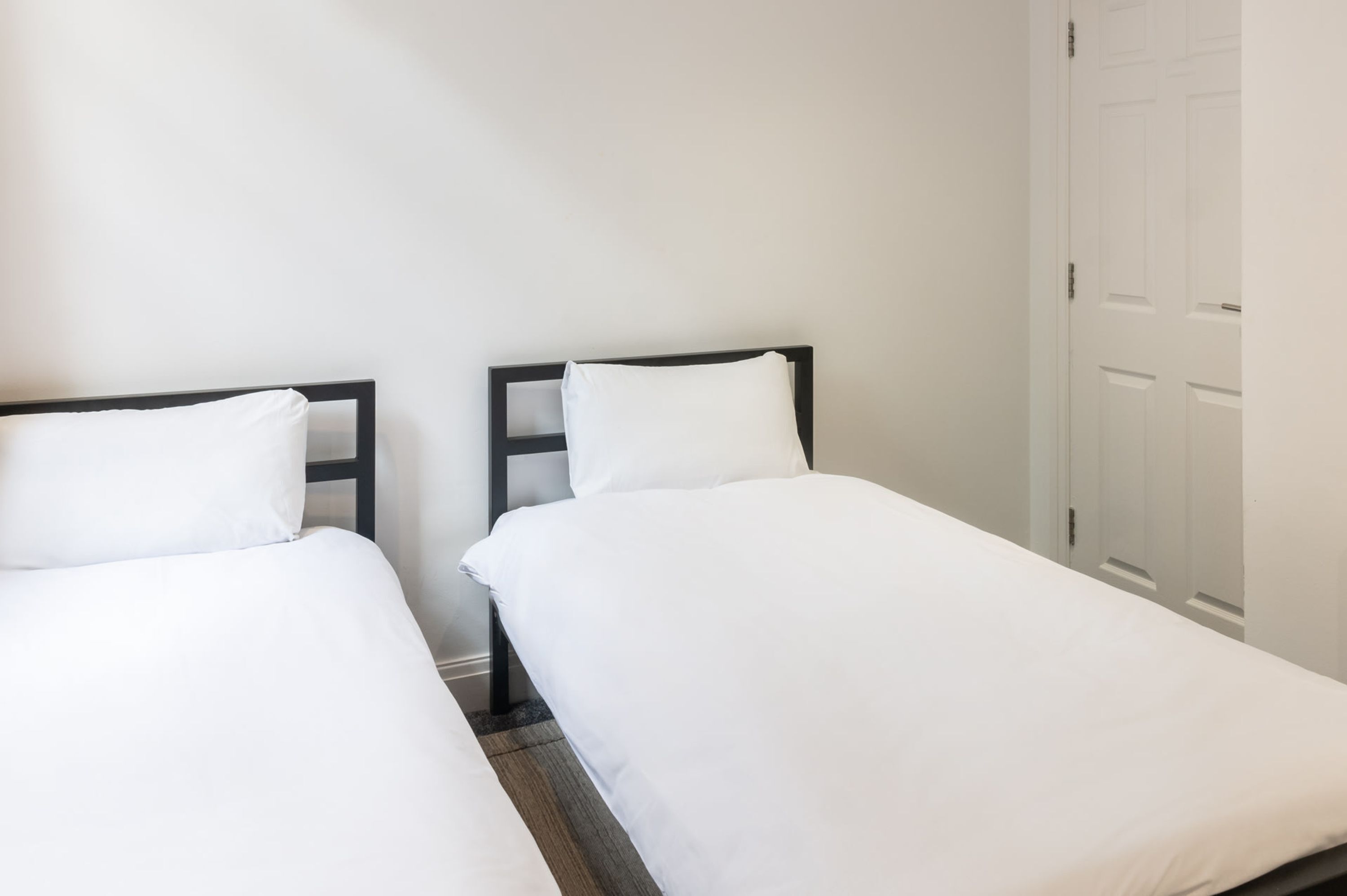 A hotel room with two single beds, white bedding, and a closed door in the background.