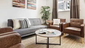 Un salon moderne avec un canapé gris, des fauteuils en cuir marron, une table basse ronde et deux tableaux abstraits accrochés au mur.
