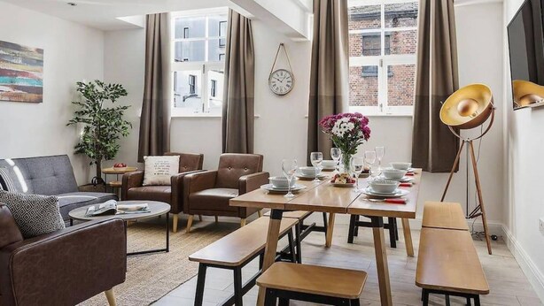 Un salon moderne comprenant un canapé, deux fauteuils, une table à manger dressée pour quatre personnes et un lampadaire.