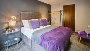 Un dormitorio con cama, mesita de noche, perchero y puerta.