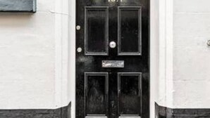 Una puerta negra con el número 18A, molduras blancas y una pequeña ventana encima.