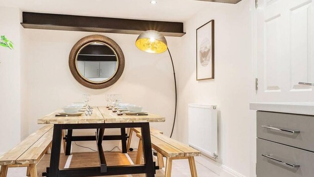 Una cocina moderna con una mesa de comedor de madera, un espejo redondo y una lámpara colgante.
