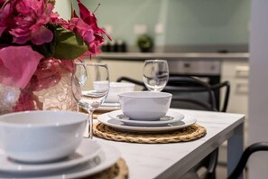 A dining table set with white bowls and glasses, a vase of pink flowers, and a woven placemat. - Host Stay The Baltic Base Apt (Liverpool)