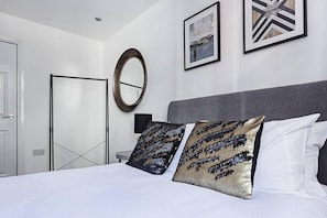 A modern bedroom with a large bed, two decorative pillows, a round mirror, and two framed pictures on the wall. - Host Stay Slater Street Apartments (Liverpool)