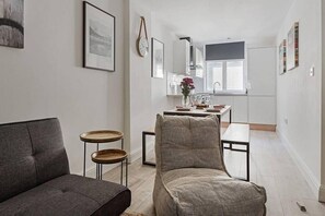 A modern living room with a grey sofa, a round wooden side table, and a grey armchair. A dining area with a table set for two is visible in the background. - Host Stay Slater Street Apartments (Liverpool)