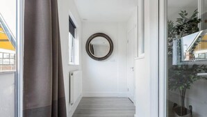 Un couloir étroit au plancher de bois, un miroir rond accroché au mur et une plante en pot sur la droite.