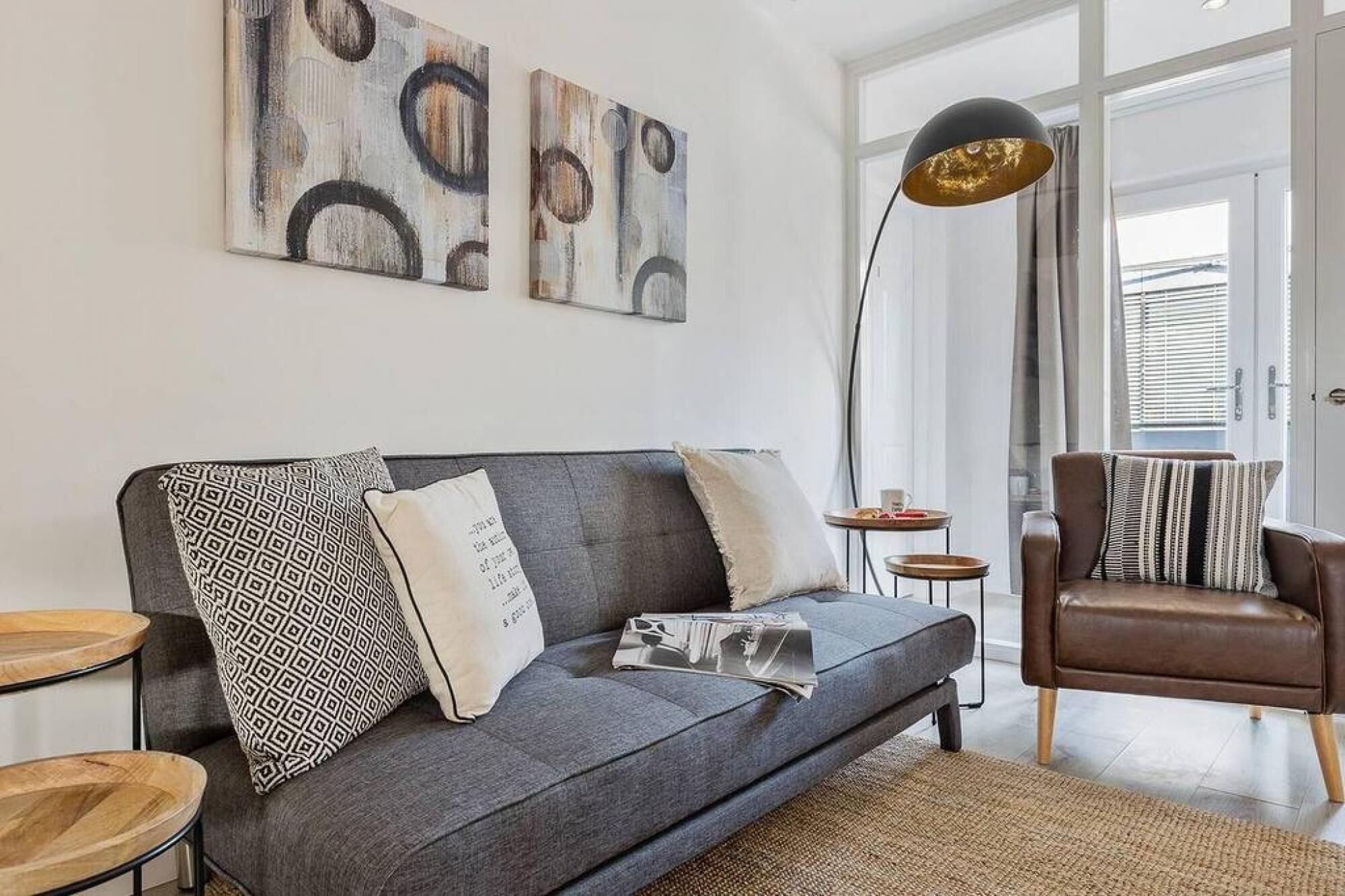 A modern living room with a grey sofa, patterned pillows, a woven rug, and abstract wall art.