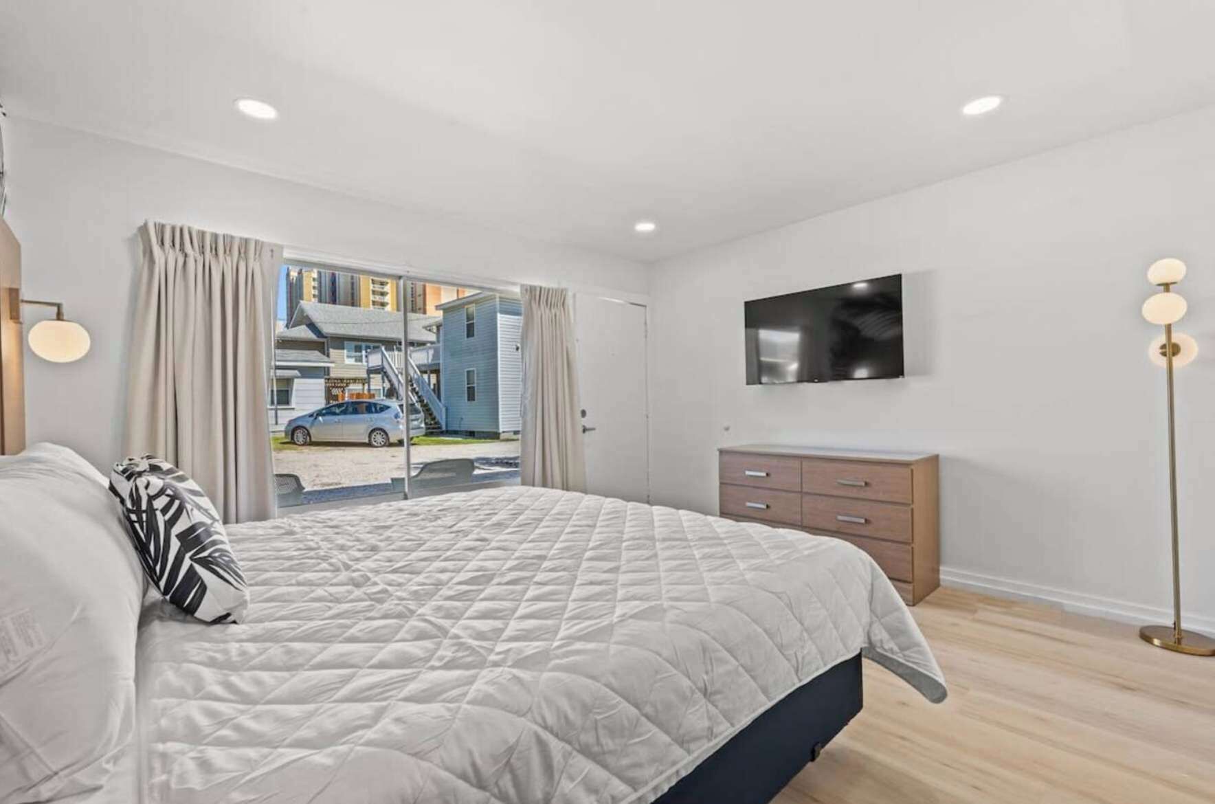 Quarto moderno com cama grande, televisão na parede e vista para o exterior.
