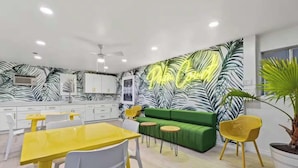 A modern kitchen with white cabinets, a yellow dining table, and a green sofa. - Sunny Studio Near the Beach at Palm Court (#10) (North Myrtle Beach)