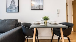A modern living room with a grey sofa, two black chairs, a small table with a plant, and two framed pictures on the wall. - Host Apartments The Pall Mall Balcony Apt (Liverpool)