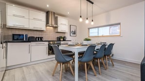 A modern kitchen with white cabinets, a stainless steel range hood, and a dining area with a white table and blue chairs. - Host Apartments Knight St Place (Liverpool)