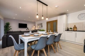 A modern kitchen with white cabinets, a dining table set for four, and a large clock on the wall. - Host Apartments Knight St Place (Liverpool)