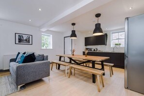 A modern kitchen with a wooden table and bench, a grey sofa, and a black pendant light. - Host Apartments The Roscoe Coach House (Liverpool)