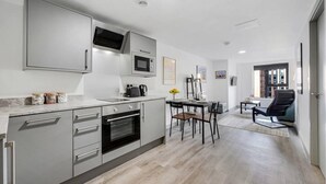 A modern kitchen with built-in appliances, a dining area with a table and chairs, and a view of the outside through a window. - Host Apartments The Roscoe Nest (Liverpool)