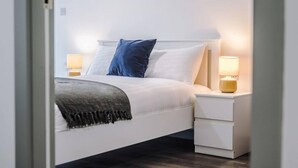 A neatly made bed with white bedding and a blue pillow, flanked by two bedside tables with lamps. - Host Apartments The Roscoe Nest (Liverpool)