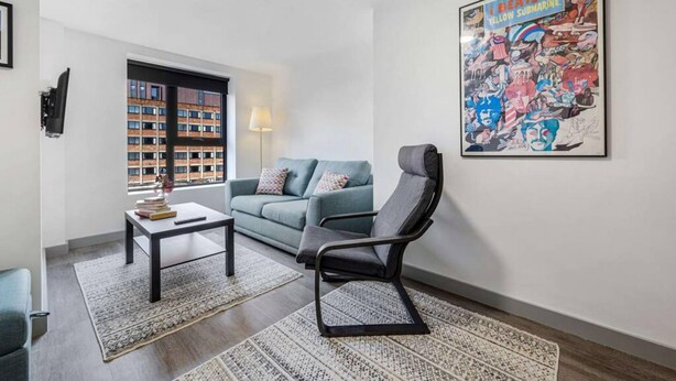 A modern living room with a sofa, a chair, a coffee table, and a large poster on the wall. - Host Apartments The Roscoe Nest (Liverpool)