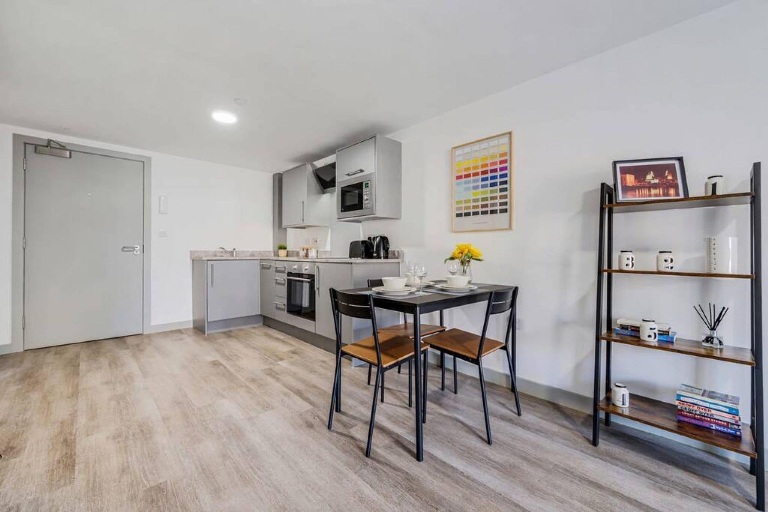 A modern kitchen with white cabinets, a microwave, and a coffee machine. There is a dining table with chairs and a small plant on the table.