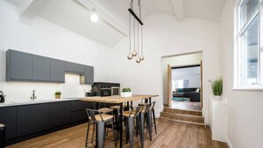 A modern kitchen with a central island, black cabinets, and a wooden dining table with chairs. - Host Apartments Wood St Nightlife Apt (Liverpool)