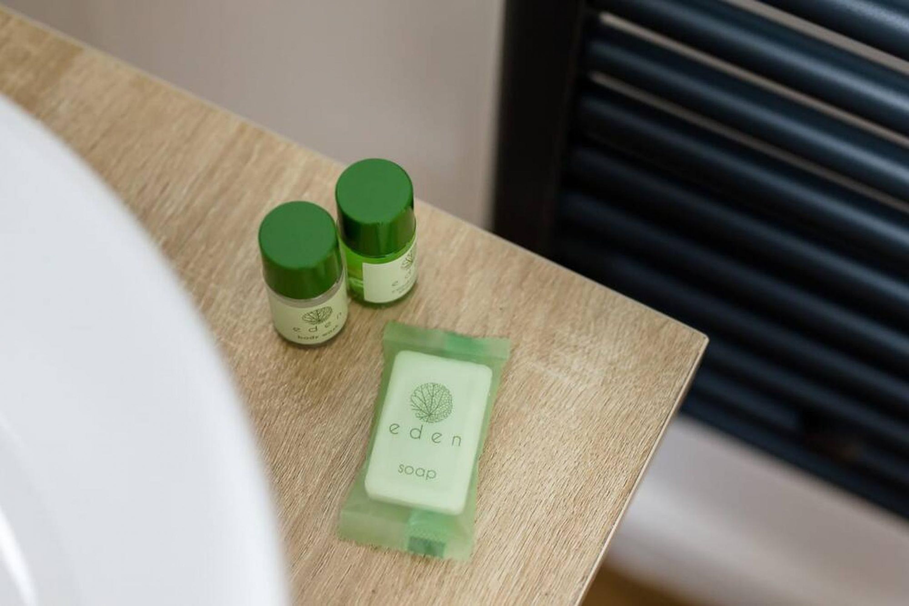 Een badkamer met een houten aanrecht, een witte wasbak en twee groene flessen met groene dopjes.