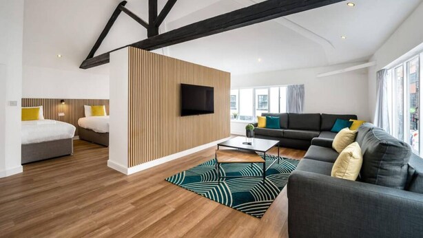 A modern living room with exposed beams, a flat-screen TV, a sofa set, and a wooden accent wall. - Host Apartments Wood St Nightlife Apt (Liverpool)