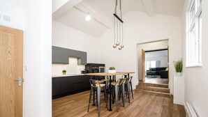 A modern kitchen with a wooden dining table and chairs, a built-in oven, and a pendant light. - Host Apartments Wood St Nightlife Apt (Liverpool)