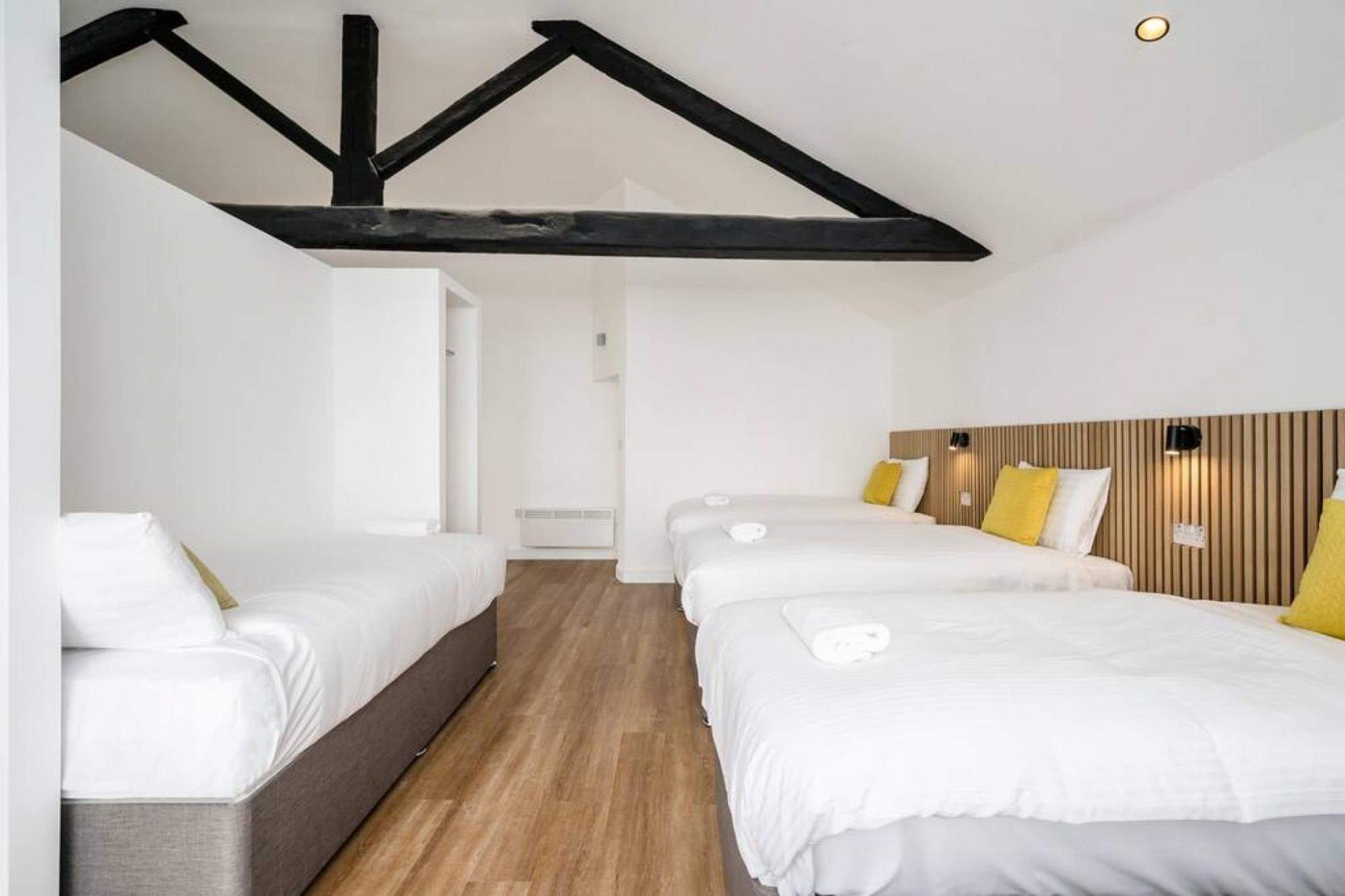 A hotel room with two single beds, a sofa, wooden flooring, and exposed black beams on the ceiling.
