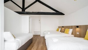 A hotel room with two single beds, a sofa, wooden flooring, and exposed black beams on the ceiling. - Host Apartments Wood St Nightlife Apt (Liverpool)