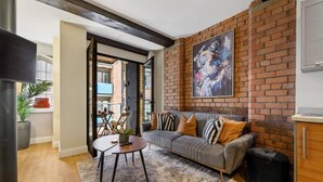 A modern living room with a grey sofa, black and white patterned cushions, a round coffee table, and a shaggy rug. A large abstract painting adorns the brick wall. - Host Apartments Queen Square Apartment (Liverpool)